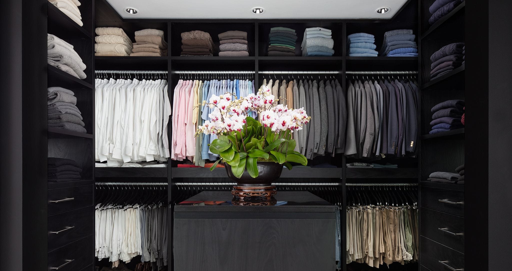 Dark wood finish walk in closet with open shelves, clothes hanging poles and center island created by California Closets